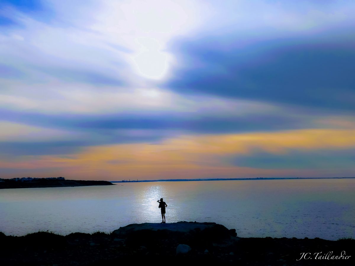 Une silhouette au bord de la mer qui se détache, au soleil couchant, sur l'horizon.